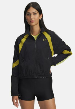 Zwarte windbreakerjas met gele diagonale strepen, ritssluiting aan de voorkant, twee zijzakken en een elastische tailleband. Lichtgewicht, soepel stof.