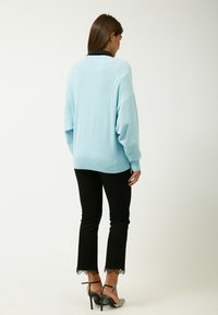 Hellblaues oversized Sweatshirt mit gerippten Bündchen und Saum, kombiniert mit schwarzen Hosen mit Spitzeneinsatz an den Knöcheln. Sichtbare Absatzschuhe.