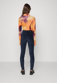 Top ajustado de manga longa com um padrão de espiral em laranja e roxo, combinado com calças de veludo cotelê de cintura alta em azul escuro. Textura suave, design elegante.