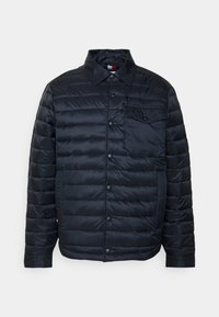 Giacca nera imbottita con chiusura a bottoni a pressione, colletto e tasca sul petto. Realizzata in tessuto lucido con motivo a trapunta verticale.