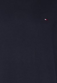 Granatowa koszulka z miękkiego materiału, z małym czerwono-białym logo na wysokości klatki piersiowej. Minimalistyczny design, krótkie rękawy.