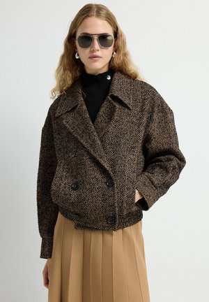 Bruin herringbone-patroon dubbelzijdig jasje met grote zwarte knopen, brede revers en een ontspannen pasvorm, gecombineerd met een geplisseerde tan rok.