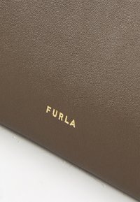 Barna, textúrált bőr felület, az aljánál arany "FURLA" logóval, amely a sima, elegáns dizájnt hangsúlyozza.