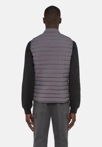 Gepolsterte graue Weste mit sleekem Design, die horizontale Steppungen, einen hohen Kragen und eine glatte Oberfläche aufweist, getragen über einem schwarzen Langarmshirt.