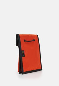 Sacchetto di tessuto arancione con accenti neri, dotato di chiusura con cordoncino e superficie testurizzata. Design compatto e pieghevole.