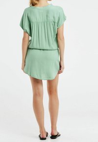 Robe courte vert menthe avec une coupe ample, des manches courtes, et un détail au dos froncé, présentant un ourlet incurvé et une texture lisse.