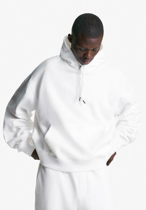 Fehér, bővebb fazonú kapucnis pulóver puha anyagból, kenguruzsebbel, húzózsinóros kapucnival, bordázott mandzsettákkal és derékpánttal. Sima tapintású anyag.