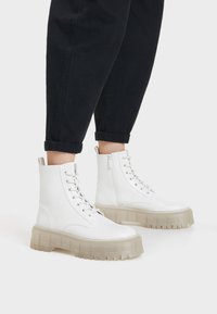 Vita ankelstövlar med en kraftig genomskinlig sula, med snörning framtill, sidodragkedja och slät lädertextur.