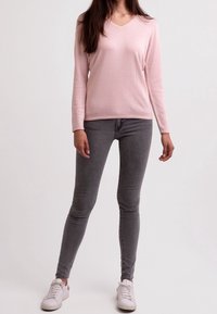 Ljusrosa långärmad v-ringad tröja i mjukt stickat tyg, som matchas med åtsittande grå jeans och vita sportskor.