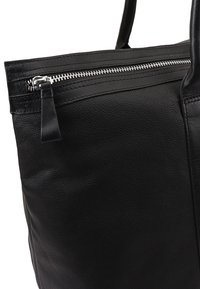 Zwarte leren tote bag met een gestructureerde afwerking, voorzien van een zilveren rits aan de bovenkant en korte, stevige handvatten.