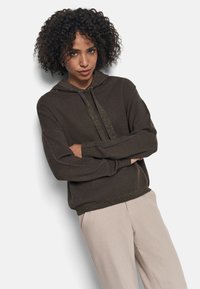 Sudadera de punto marrón con un cordón brillante, puños y dobladillo acanalados. Combinada con pantalones beige claros. Textura suave, corte relajado.