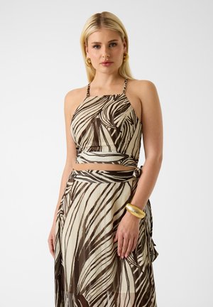 Donna bionda che indossa un top corto a stampa zebra marrone e beige con collo allacciato al collo e gonna coordinata, accessoriata con orecchini a cerchio dorati e braccialetto rigido.