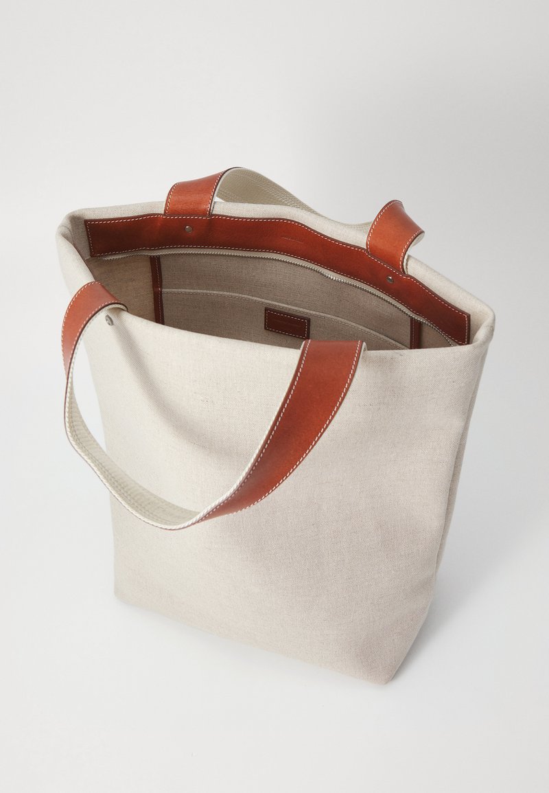 Leichter beigefarbener Canvas-Shopper mit braunen Ledergriffen. Verfügt über ein geräumiges Innenleben und Kontrastnähte entlang der Kanten.