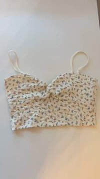 Floral crop top with a twisted front design, white fabric, small multicolored flowers, and thin adjustable straps. Textured surface.