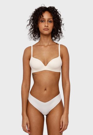 Reggiseno beige imbottito con spalline regolabili e scollatura profonda, abbinato a un perizoma bianco a vita alta, con texture liscia.