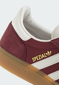 Bordó szarvasbőr sneaker fehér bőr részletekkel. Arany színű "SPEZIAL" felirattal és három fehér csíkkal rendelkezik. Átlátszó gumitalppal, amely texturált mintával bír.
