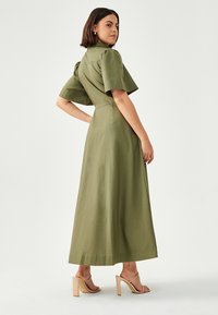 Sukienka maxi w oliwkowym kolorze, uszyta z materiału z krótkimi, bufiastymi rękawami oraz dopasowaną talią, charakteryzująca się gładką fakturą i wykończeniem bez zagnieceń.