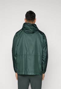 Green hooded jacket with a smooth, shiny texture. Features elastic cuffs and a cinched waist, designed for a relaxed fit.