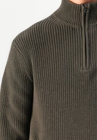 Maglione a maglia verde oliva scuro con colletto alto e breve zip, caratterizzato da una texture a righe verticali e design aderente.
