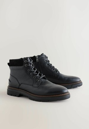 Svarta läderstövlar med strukturerad yta, rund tå och snörad design. Har dragkedjestängning och kontrasterande bruna sömmar på sulan.