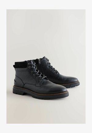 Black leather boots with a textured finish, round toe, and laced design. Features a zip closure and contrasting brown stitching on the sole.