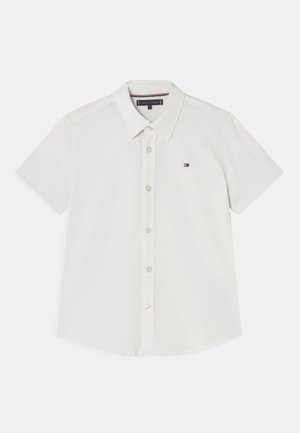 Biała koszula z krótkim rękawem wykonana z gładkiej tkaniny. Posiada klasyczny kołnierzyk, zapięcie na guziki z przodu oraz małe haftowane logo na piersi.