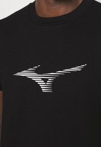 Czarna bawełniana koszulka z dopasowanym krojem, z białym prążkowanym logo w kształcie stylizowanej litery M na klatce piersiowej.