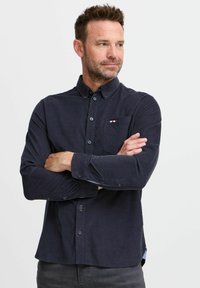 Navyblauw overhemd met lange mouwen en een button-down kraag, voorzien van een borstzak met een rood, wit en blauw accent, en knoopmanchetten.