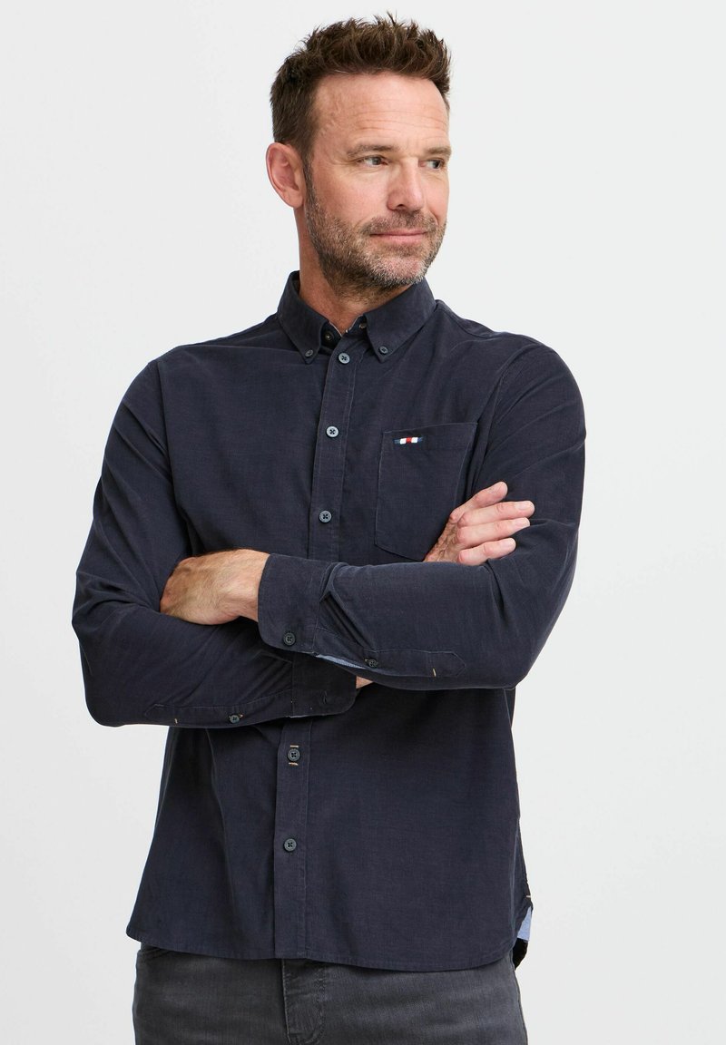 Navyblauw overhemd met lange mouwen en een button-down kraag, voorzien van een borstzak met een rood, wit en blauw accent, en knoopmanchetten.