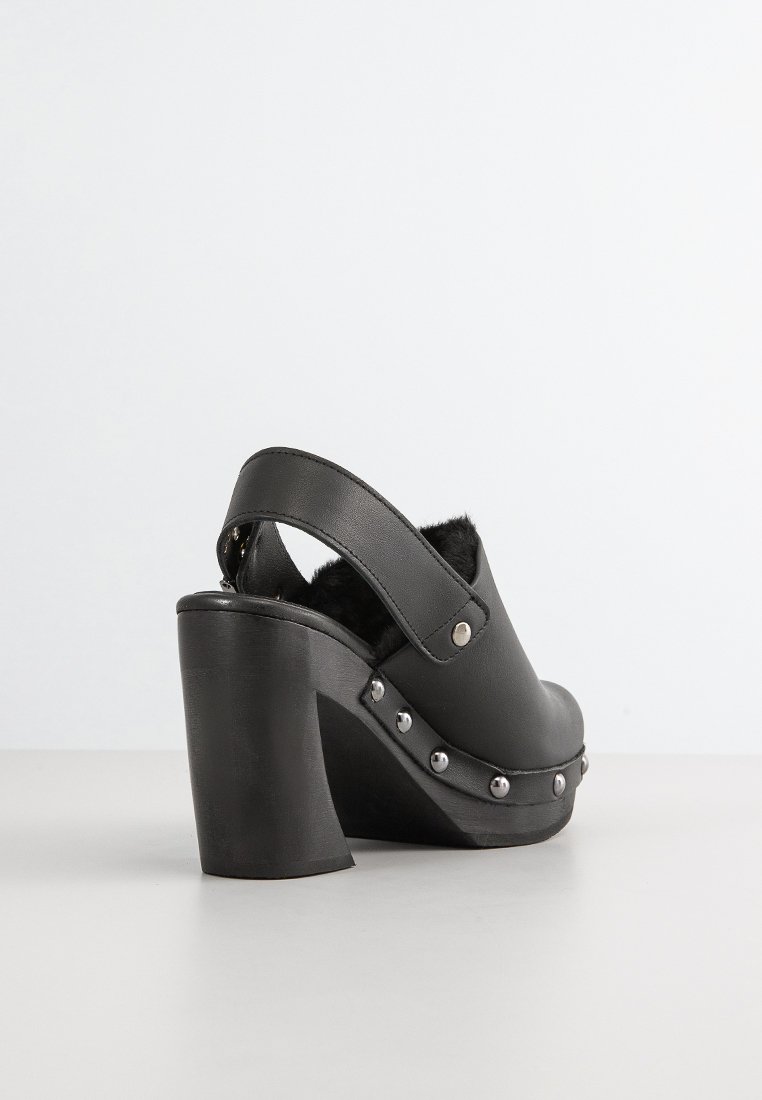 Schwarze Absatzschuhe im Clog-Stil mit runder Zehenpartie, Kunstfellfutter und silbernen Nietenverzierungen an der Seite. Klobiger Absatz und Riemen Design hinten.