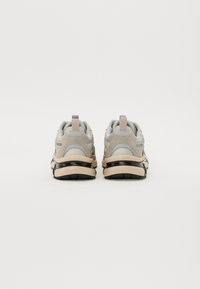 Beżowe i szare sneakersy mają gładką cholewkę z miękkiej skóry i zamszu, wyściełany kołnierz oraz kontrastującą czarną podeszwę. Subtelne logo po boku.
