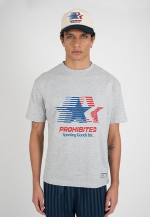 Hombre con camiseta gris y gorra de béisbol crema, ambas con un logo de estrella roja y azul y el texto "PROHIBITED Sporting Goods Inc.".
