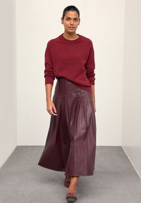 Bourgognefarvet striktrøje med rund hals kombineret med en plisseret, højtaljet lædernederdel i en matchende bourgognefarve. Inkluderer afslappet fodtøj.