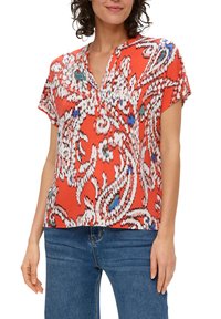 Kurzarmbluse in leuchtendem Rot mit Paisleymuster, ausgestattet mit einem Ausschnitt und weichem, strukturiertem Material. Kombiniert mit blauen Jeans.