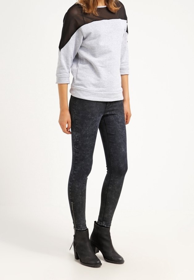 Felpa grigia con sovrapposizione sheer nera, abbinata a jeans skinny in denim scuro con finitura strappata e dettagli con zip. Stivaletti neri.