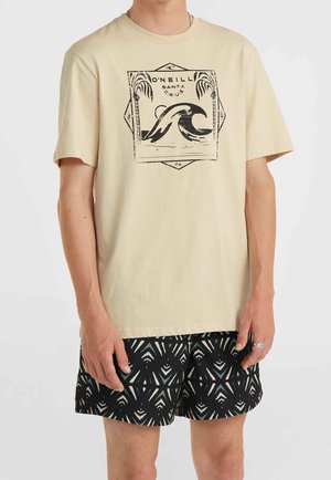 Beige Baumwoll-T-Shirt mit einem schwarzen Wellenmotiv und Akzenten von Palmen. Kombiniert mit schwarzen Shorts, die ein geometrisches Muster in Türkis und Weiß aufweisen.
