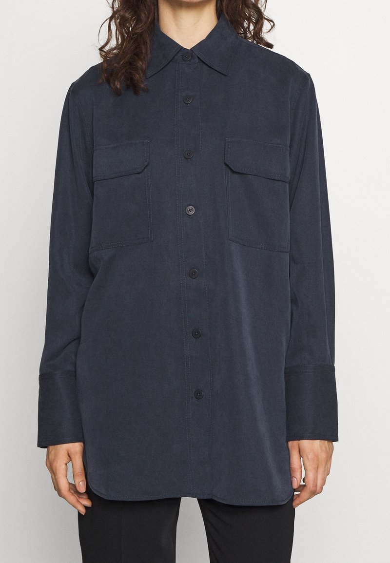 Chemise bleu marine à manches longues en tissu doux, avec fermeture à boutons, col pointu et deux poches poitrine à rabats.