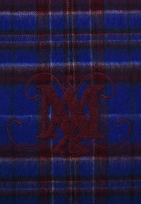 Blå og rød rutet stoff med en myk, teksturert finish. Inkluderer et brodert burgunder monogram sentrert på designet.