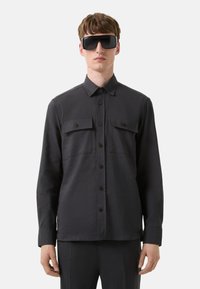 Donkergrijze langemouwen shirt met een knoopsluiting aan de voorkant, twee borstzakken en bruine knopen. Glad stof met een gestructureerde pasvorm.