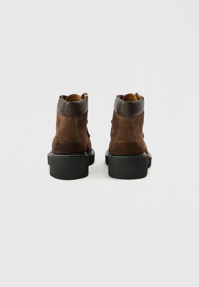 Barna velúr bokacsizma sötétbarna bőrgallérral, fekete gumitalppal és az él mentén látható varrási részlettel.