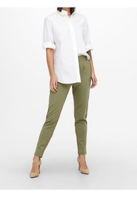 Bílá košile s knoflíky a ohrnutými rukávy, doplněná o olivově zelené úzké kalhoty a nahé vysoké podpatky. Hladká látka s klasickým designem.