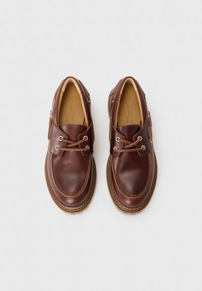 Scarpe in pelle marrone con punta arrotondata, dettagli cuciti e lacci a contrasto. Suola in gomma spessa con battistrada testurizzata per una presa migliore.