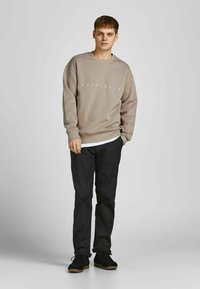 Lichtgrijze sweatshirt met de tekst "ORIGINALS", gecombineerd met zwarte broek en zwarte schoenen. Casual pasvorm, eenvoudig ontwerp en zachte textuur.
