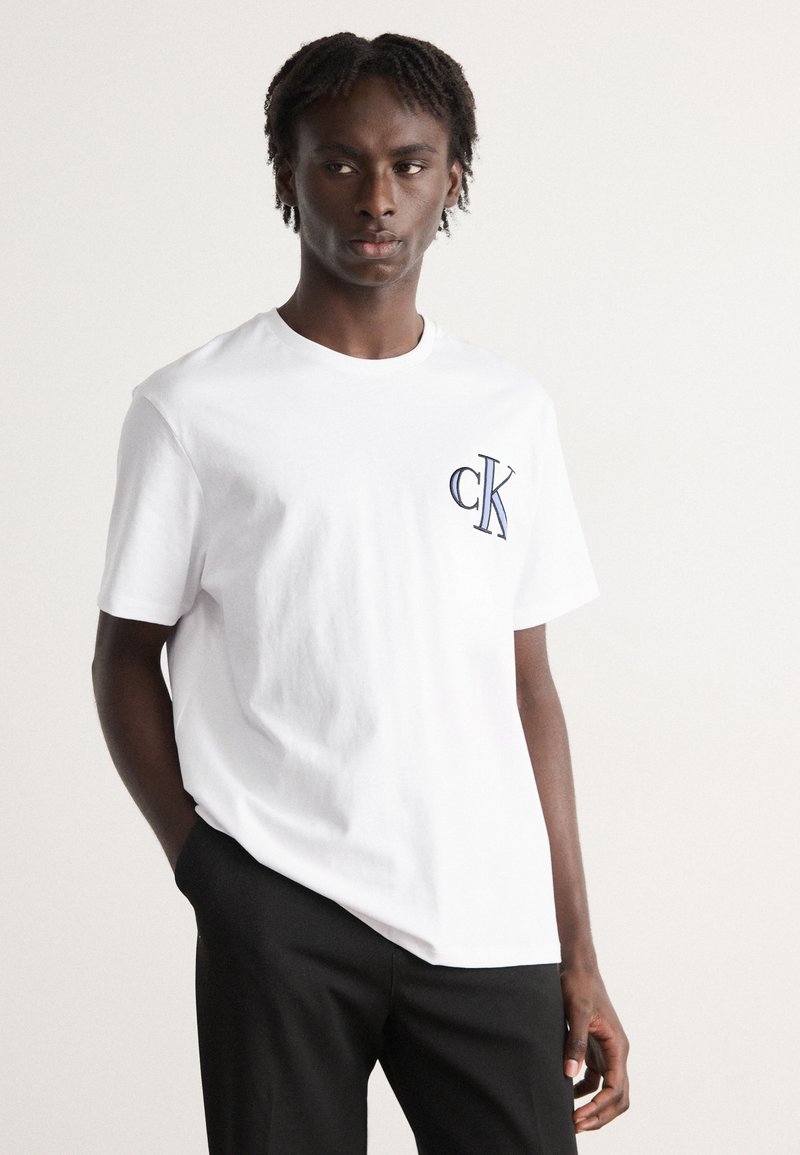 Hvid bomulds t-shirt med et blåt broderet "CK" logo på venstre bryst. Standard rund halsudskæring og korte ærmer.