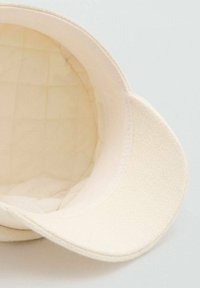 Cremfarbener Bucket Hat mit strukturiertem Außenstoff, weicher, gestepptem Innenfutter und breiter, geteilter Krempe.