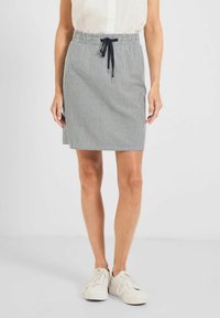 Falda de longitud hasta la rodilla a rayas en gris y blanco, con una cinturilla elástica y un cordón negro. Combinada con zapatillas blancas.