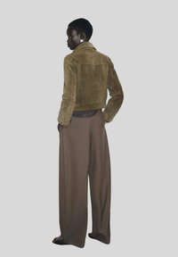 Veste en daim vert olive avec un design cropped, associée à un pantalon marron ample, mettant en valeur une finition texturée et des détails simples.