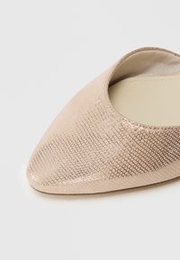 Sandală bej cu vârf ascuțit, având o suprafață texturată ce semănă cu hexagoane mici, interior neted și laterale deschise pentru o purtare ușoară.