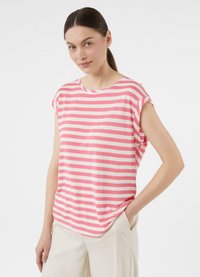 Różowa i biała w paski koszula z krótkim rękawem o okrągłym dekolcie, luźny fason i miękki materiał bawełniany. Noszona z jasnobezowymi spodniami.