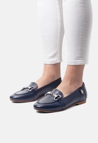 Marinblå lädersandaler med silverdetaljer, rund tå och en lågprofil-design. Matchas med vita avskurna jeans.